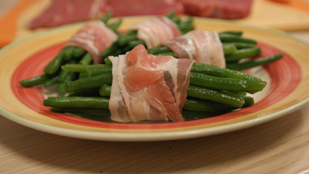 An image of a plate of green beans wrapped with bacon.